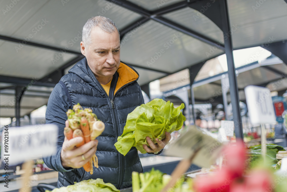 Fototapeta premium Mature man picking vegetables at farmers's market. Man buying organic fruits and vegetables at an open street market. Local Farmers Market. Fresh produce: vegetables