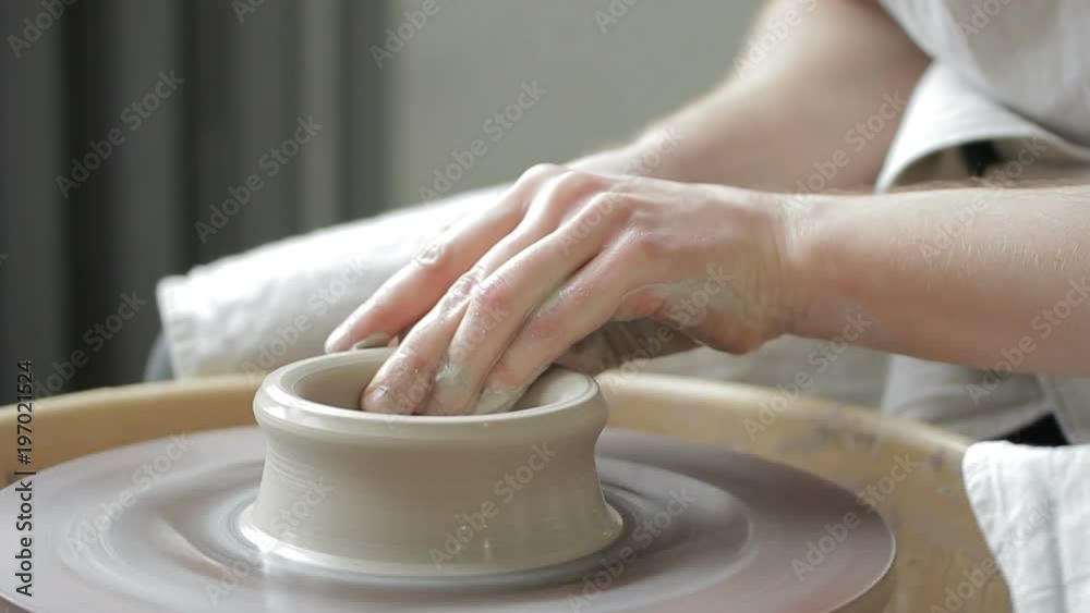 Process of creating dishes on a rotating potter's wheel by hand. Close-up mens hands of the master are quickly shaped into bowls of clay mass and water.