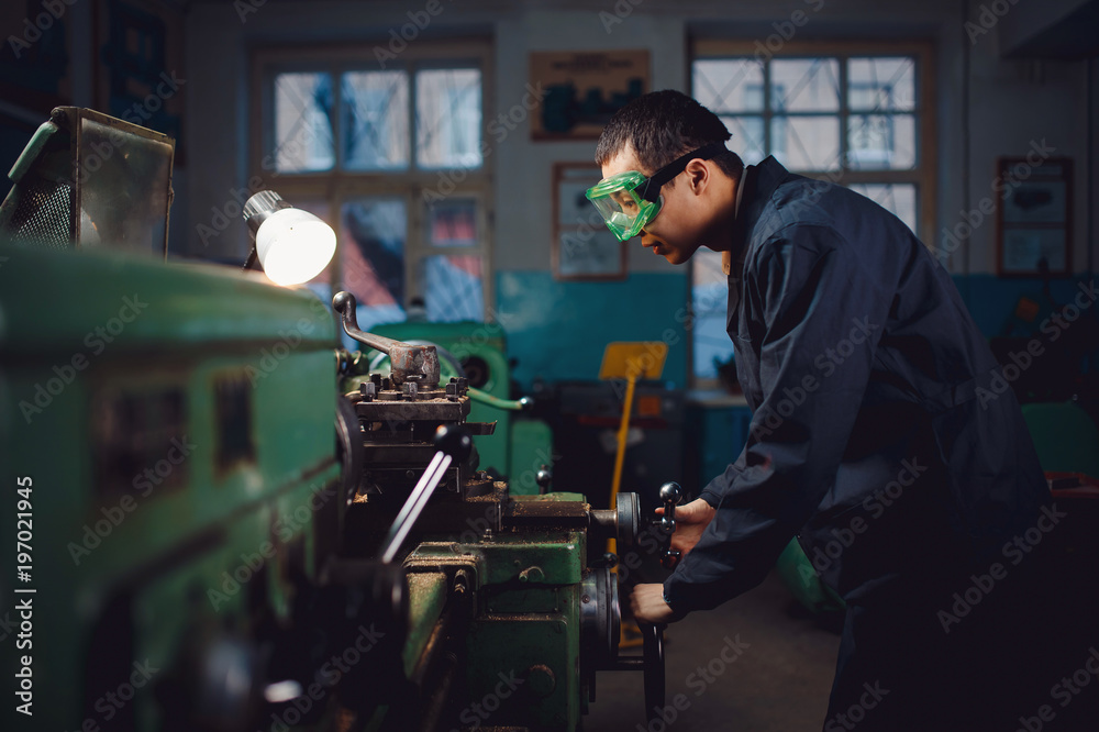 Engineer turner Asian man stands in goggles behind automatic machine. Concept industrial worker for production of metal structures. Engineer turner Asian man stands in goggles behind automatic machine. Concept industrial worker for production of metal structures.