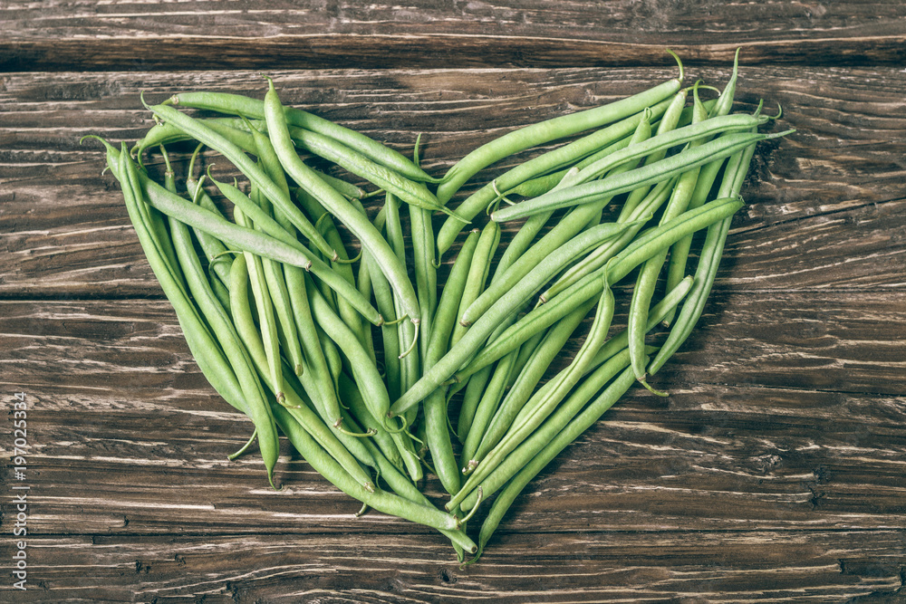 Heart of green beans on a rustic wooden  table top view.