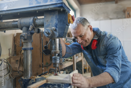 Mature carpenter using drill press in workshop