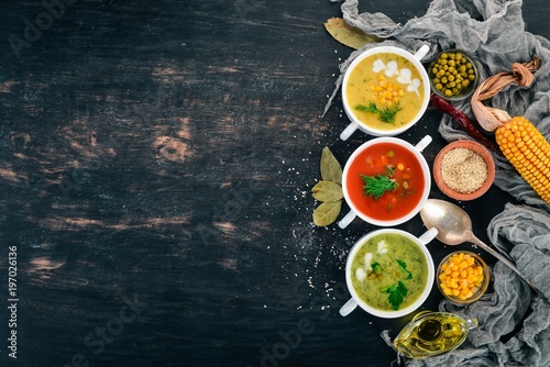 Set of hot, colored vegetable soups. Broccoli soup, corn, tomato soup. Healthy food. On a black wooden background. Copy space.