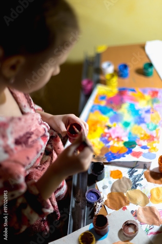 Cute little girl painting with paintbrush and colorful paints in home interior