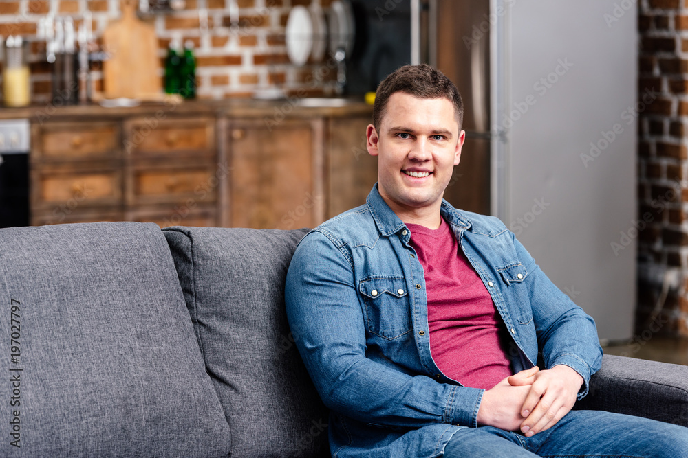 handsome young man sitting on couch and smiling at camera handsome young man sitting on couch and smiling at camera
