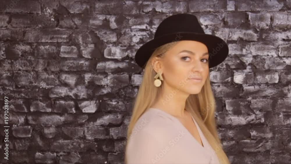 A girl in a black hat and a gray shirt posing against a brick wall background A girl in a black hat and a gray shirt posing against a brick wall background