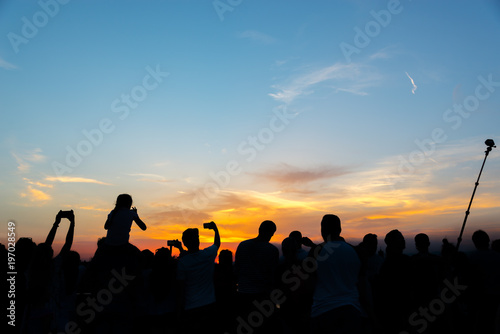 Crowd of people taking pictures of the sunset with mobile phones and selfie stick on a summer night in Florence, Italy © Delphotostock