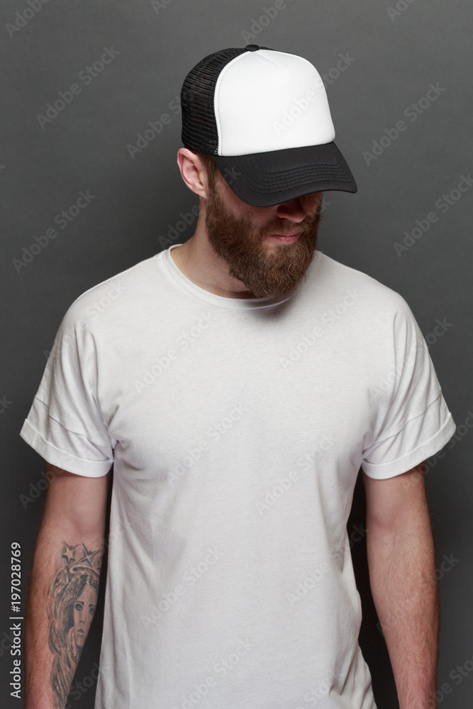 Hipster handsome male model with beard wearing white blank t-shirt and a baseball cap with space for your logo or design in casual urban style Hipster handsome male model with beard wearing white blank t-shirt and a baseball cap with space for your logo or design in casual urban style