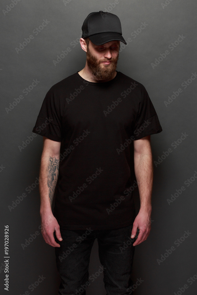 Hipster handsome male model with beard wearing black blank t-shirt and a black baseball cap with space for your logo or design in casual urban style Hipster handsome male model with beard wearing black blank t-shirt and a black baseball cap with space for your logo or design in casual urban style