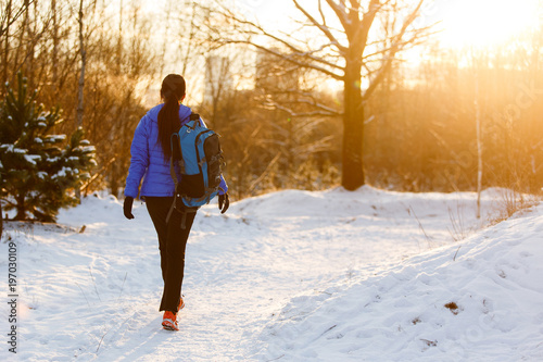 Image from back of walking sports woman with backpack in winter forest