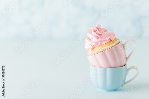 Cupcake with pink buttercream decoration in two cups on blue pastel background.