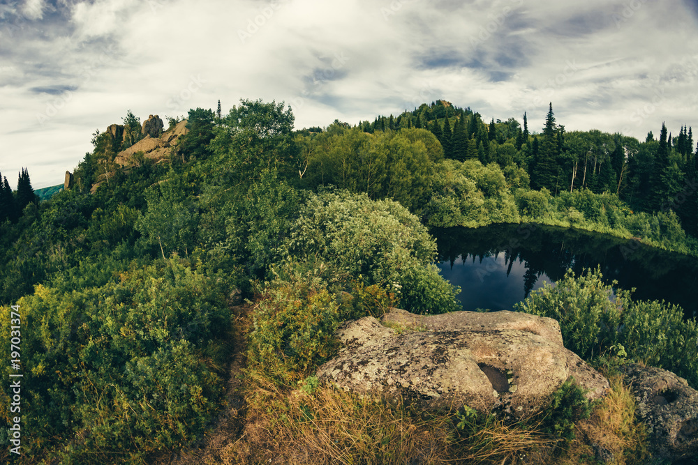 Obraz premium Lake on top of hill, surrounded by rocks and thickets, captured by the fisheye lens.