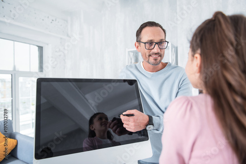 Modern electronics. Positive pleasant nice man standing near the digital screen and showing it to his daughter while talking to her