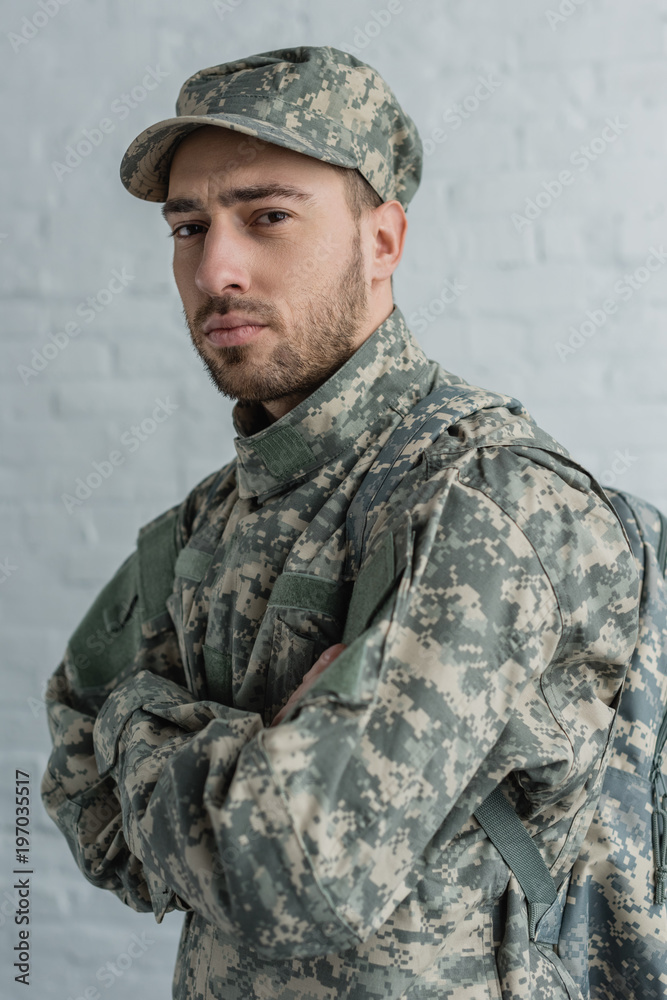 portrait of soldier in military uniform looking at camera against white brick wall