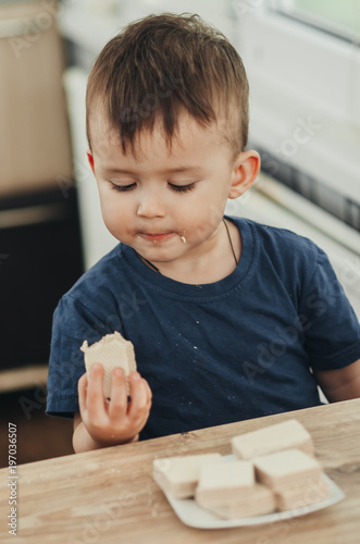 a little charming boy eats waffles in the kitchen and drinks milk photo