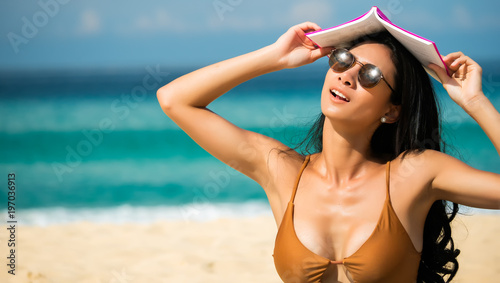 Sexy asian woman sunbathing with book on head on the beach with beautiful beach background  While relaxing on weekends in travel and holiday concept.