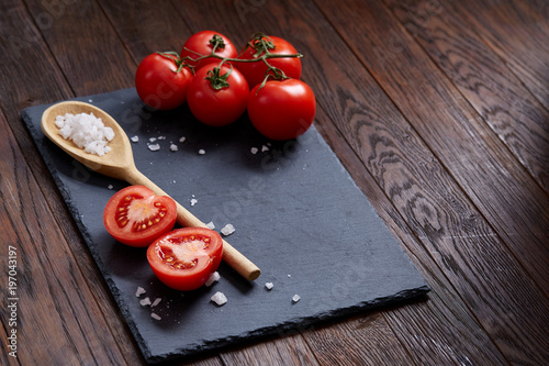 Vegetarian still life with fresh grape tomatoes, pepper and salt in wooden spoon on wooden background, selective focus