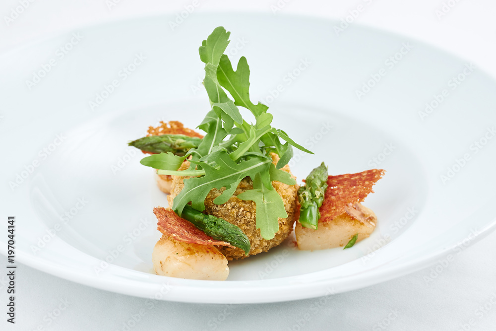 Delicious meal. Dish with pieces of grilled fish, rusks, green leaves of arugula and asparagus on a white plate. Delicious meal. Dish with pieces of grilled fish, rusks, green leaves of arugula and asparagus on a white plate.