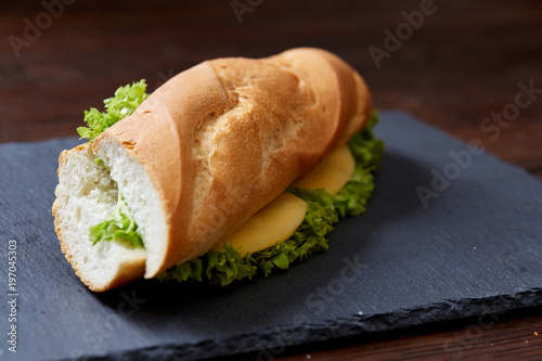 Fresh and tasty sandwich with cheese and vegetables on cutting board over wooden background, selective focus.