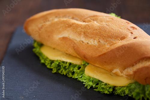 Fresh and tasty sandwich with cheese and vegetables on cutting board over wooden background, selective focus.