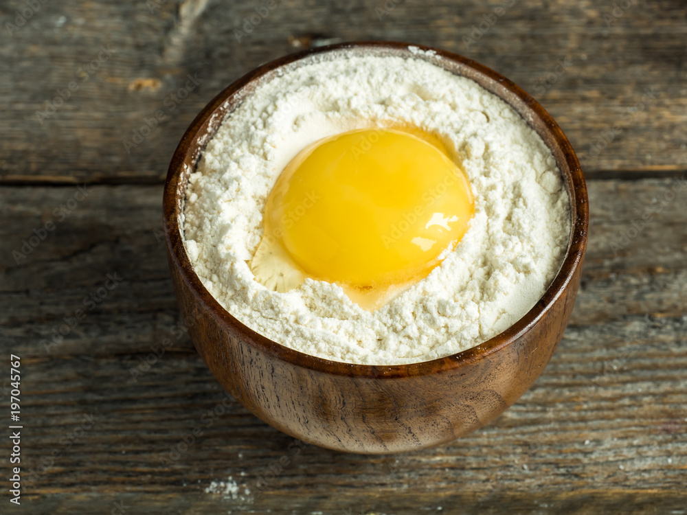 Wooden bowl with flour and broken chicken egg on rustic background Wooden bowl with flour and broken chicken egg on rustic background