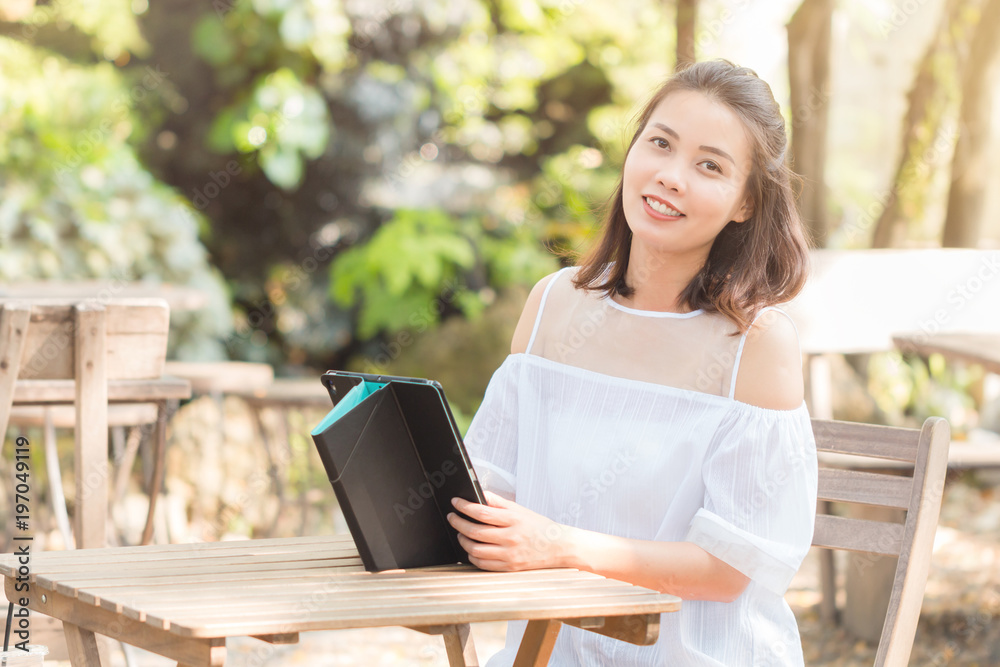 Obraz premium Portrait of Attractive young Asian woman wearing white casual using tablet smiling and looking at camera. Technology, Internet, and Business concept.