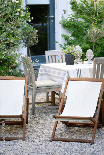 White loungers and table covered with white, gray and beige linen on a gravel terrace for a relaxing summer break photo