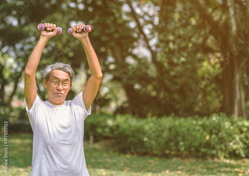 Asian mature man lifting dumbbell on natural background.