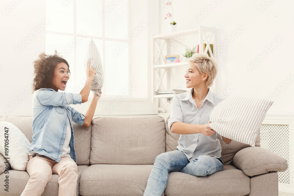 Two young women having pillow fight on sofa