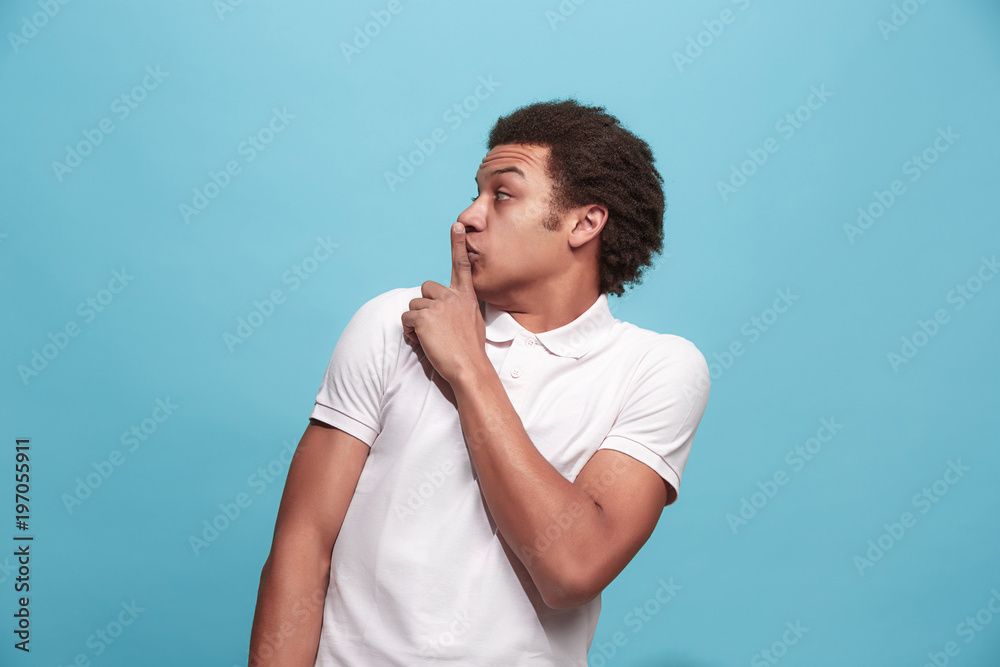 The young man whispering a secret behind her hand over blue background The young man whispering a secret behind her hand over blue background