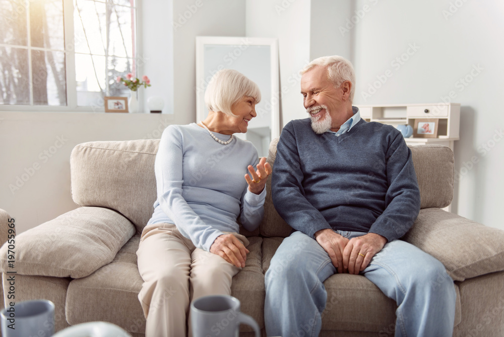 Having fun together. Cheerful elderly couple sitting on the couch in the living room and laughing while cracking jokes together Having fun together. Cheerful elderly couple sitting on the couch in the living room and laughing while cracking jokes together