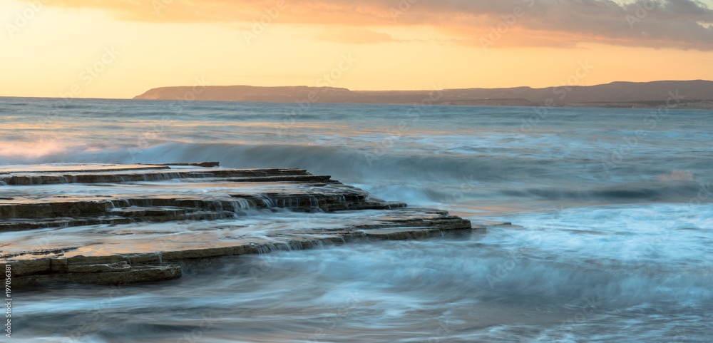 Rocky seashore seascape with wavy ocean during sunset