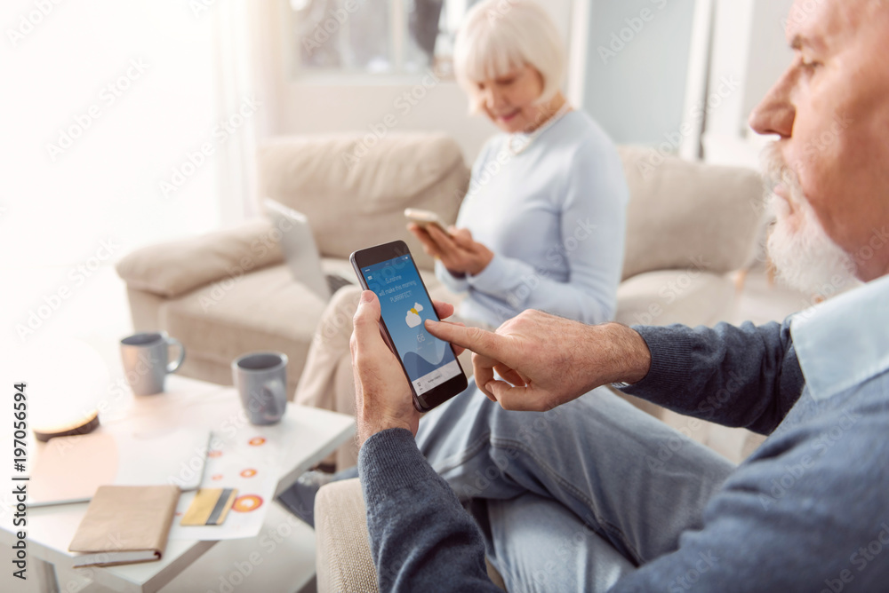 Useful app. The focus being on a bearded elderly man sitting in the armchair in the living room and checking the weather forecast in the application on his phone