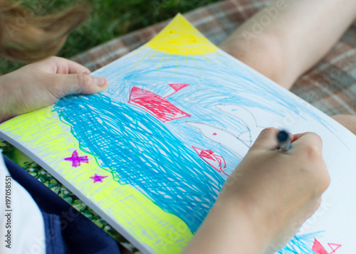 A little girl paints with felt-tip pens in the album. A close-up photo