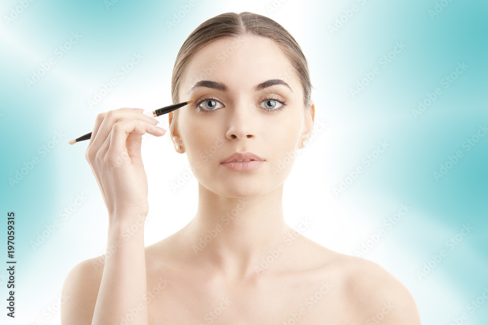 Studio shot of a beautiful young woman applying makeup to her eyebrow while standing at isolated background.