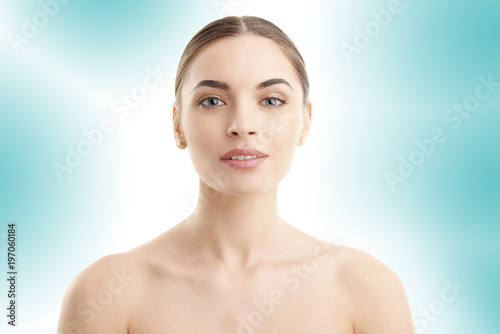 Flawless beauty. Close-up portrait of an attractive woman with perfect skin looking at camera while posing against at isolated light blue background. 