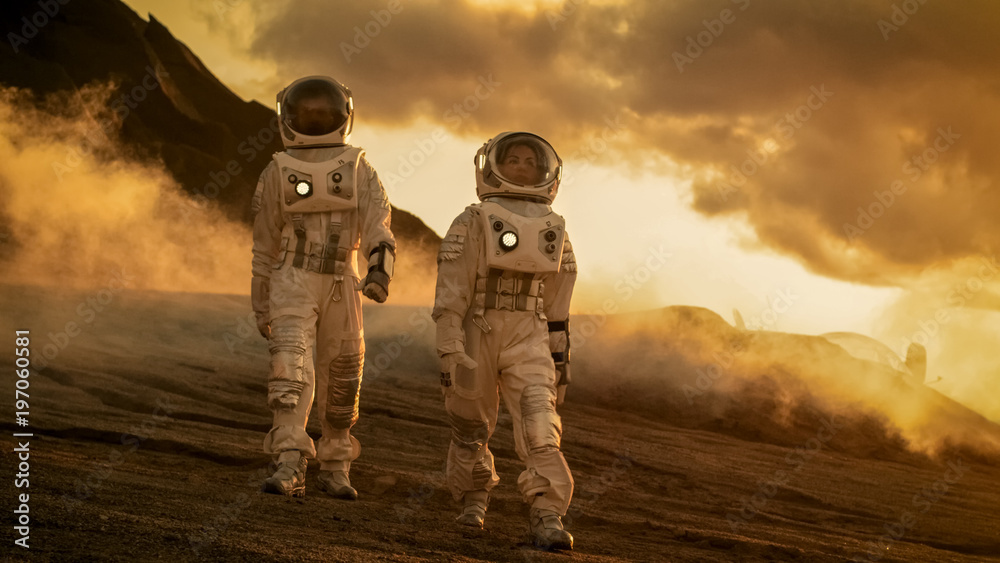 Two Astronauts in Space Suits Confidently Walking on Mars, Exploration Expedition on the Planet's Surface. Red Planet Covered in Rocks, Gas and Smoke. Humans Overcoming Difficulties. Two Astronauts in Space Suits Confidently Walking on Mars, Exploration Expedition on the Planet's Surface. Red Planet Covered in Rocks, Gas and Smoke. Humans Overcoming Difficulties.