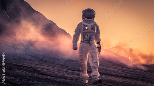 Astronaut Wearing Space Suit Walks on the Red Planet/Venus During Sunset. In the Background His Base with Rover Parked, Hot Red Daylight Sun Shines.