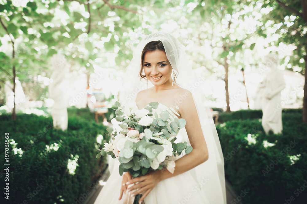 Beautiful brunette bride in elegant white dress holding bouquet posing neat trees Beautiful brunette bride in elegant white dress holding bouquet posing neat trees
