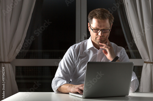 Mann denkt nach, während er einen neuen Blogartikel am Notebook in seinem Home Office verfasst photo