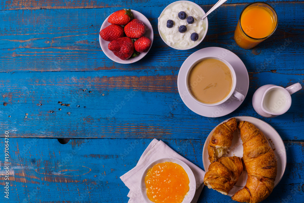 Healthy morning breakfast  served  with croissants, coffee,  fruit juice, milk, fruit jam, orange, on old blue wooden background, flat lay view, with copy space.