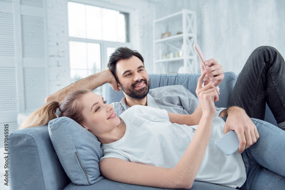 Young couple. Relaxed blonde expressing positivity while spending time with her boyfriend and looking at her gadget Young couple. Relaxed blonde expressing positivity while spending time with her boyfriend and looking at her gadget