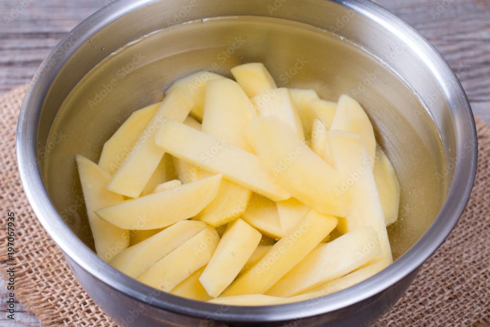 Sliced potatoes in water in a metal bowl