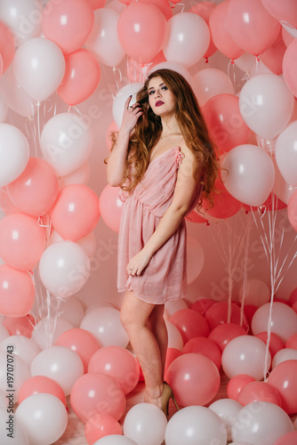 Beautiful young girl in a dress among a lot of pink balls.