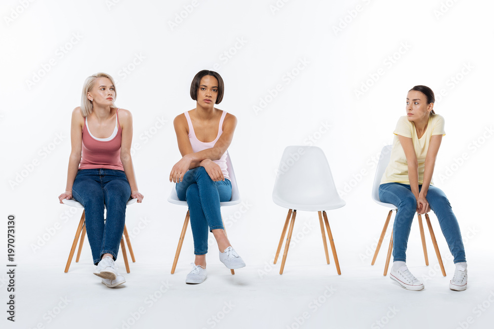 Obraz premium Special project. Serious nice young women sitting on the chair and waiting for their friend while participating in the social project