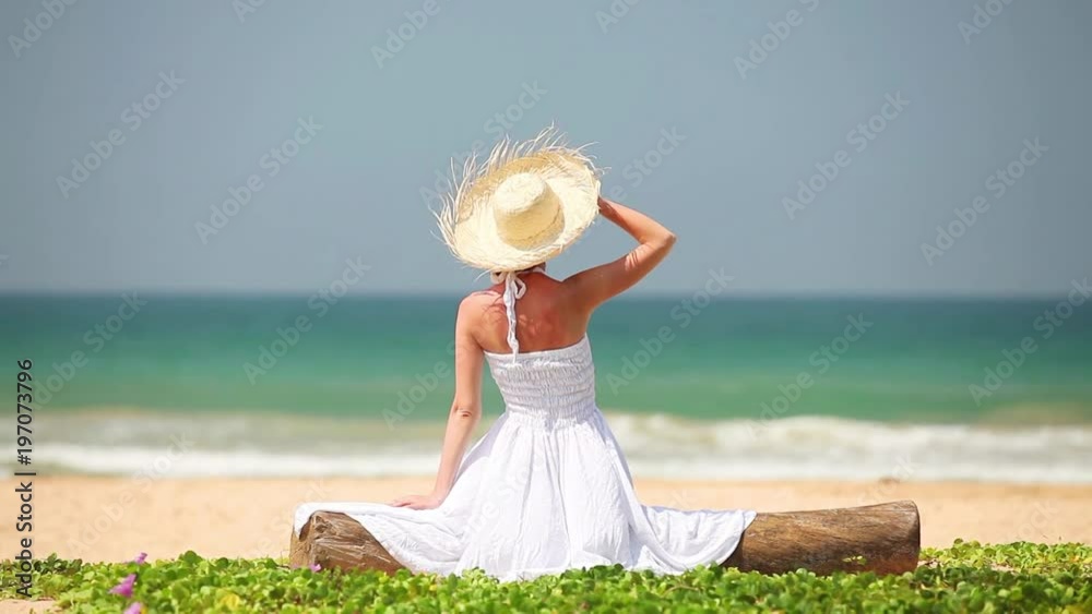 Young girl in hat and white dress sitting on the beach in summerime Young girl in hat and white dress sitting on the beach in summerime