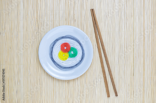 Colorful strings in form of sushi on white plate and sticks isolated on beige bamboo straw mat background