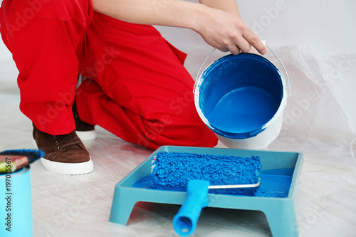 Male decorator pouring paint into tray indoors