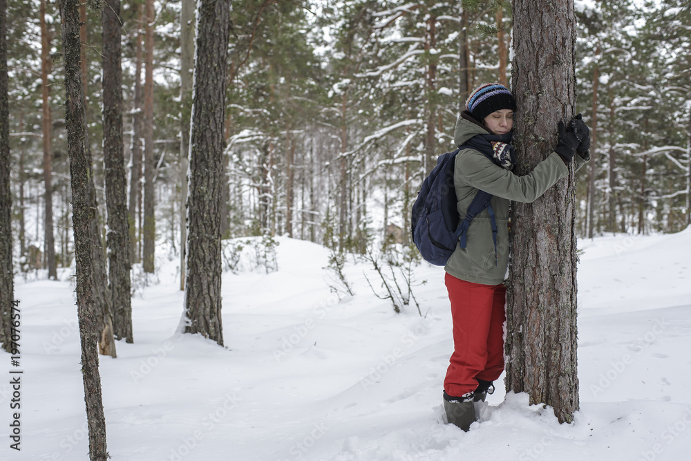 Cute woman hugging a tree in the winter forest. The concept of conservation of nature.