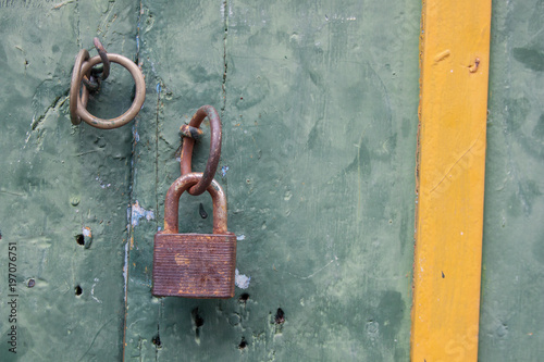 Weathered exterior door. Green door with closed rusty padlock. Non secure concept. Grunge wooden textured door background, wallpaper. photo