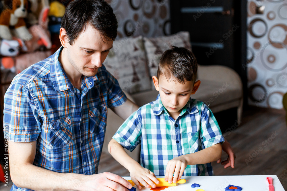 Fototapeta premium Picture of a father and a son playing with color play dough and cutters. Having fun with colorful modeling clay. Creative kids molding at home. Children play with plasticine or dough.